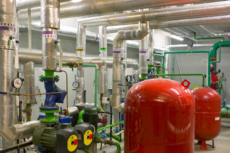 Inside of large boiler room showing lots of complicated industrial sized pipework and a couple of boiler cylinders and pumps
